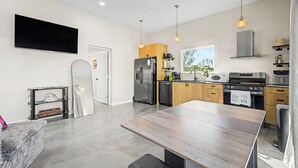 Une cuisine moderne dotée d’un grand îlot central, d’appareils électroménagers en acier inoxydable et de luminaires suspendus.