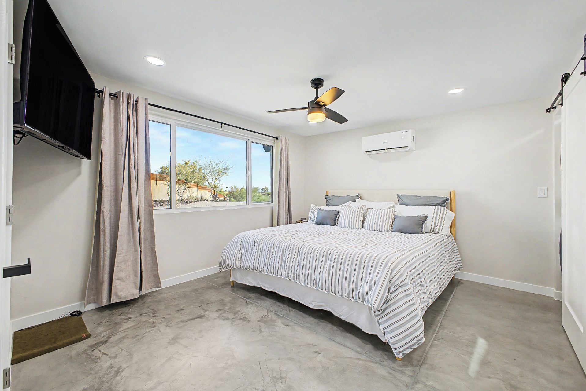 Une chambre à coucher avec un lit, un ventilateur de plafond, une fenêtre et un appareil de climatisation.