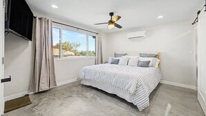Une chambre à coucher avec un lit, un ventilateur de plafond, une fenêtre et un appareil de climatisation.