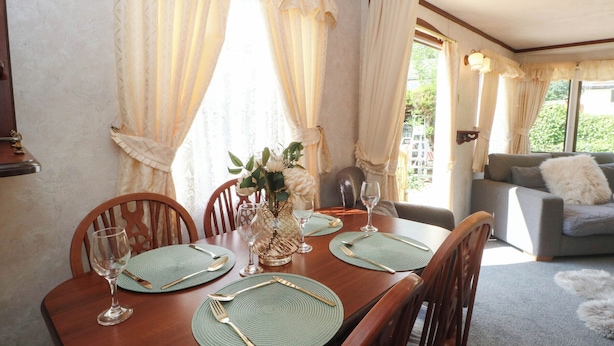 A dining area with a wooden table set for four, surrounded by chairs, with a vase of flowers on the table.