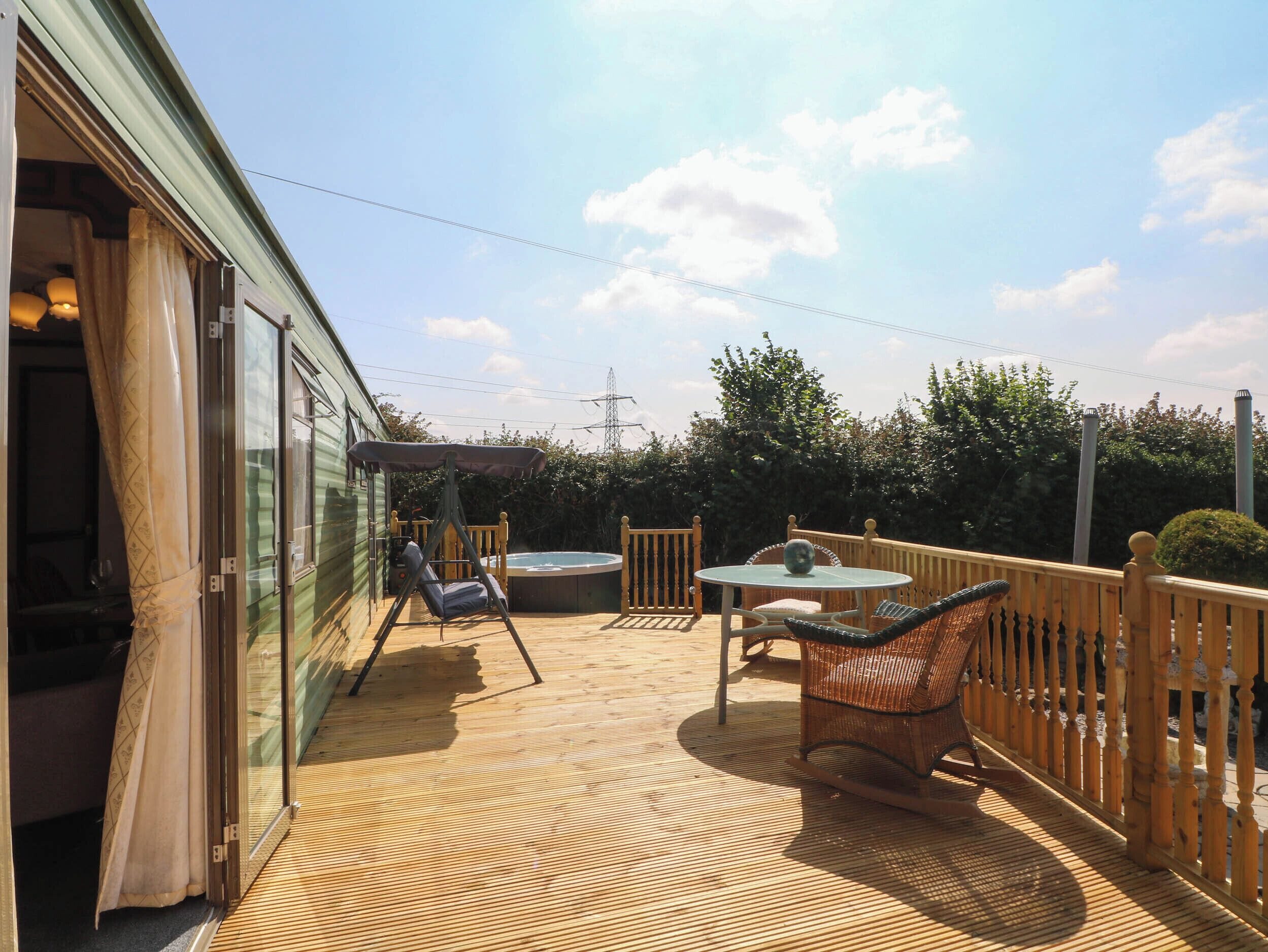 Una terraza de madera con un jacuzzi, sillas de mimbre y una mesa.