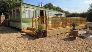 A green mobile home with a wooden deck and potted plants.