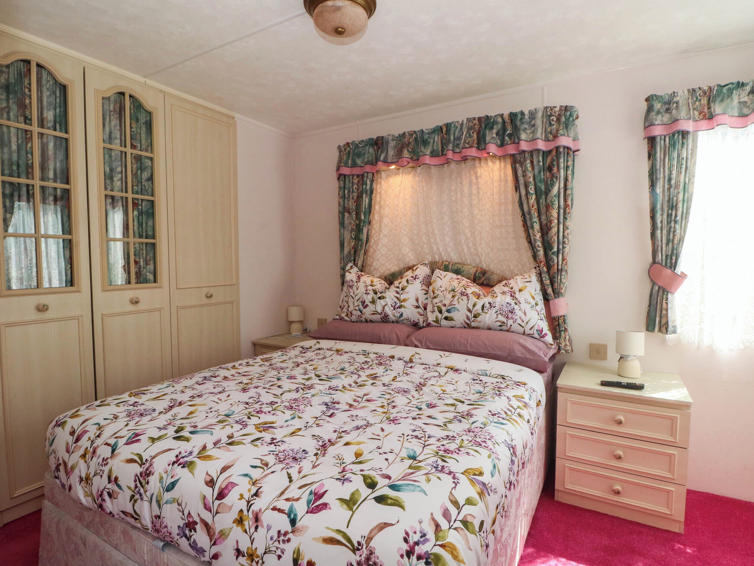 A bedroom with a bed, a nightstand, a dresser, and a window with curtains.