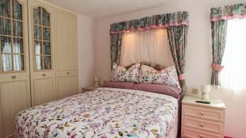 A bedroom with a bed, a nightstand, a dresser, and a window with curtains.