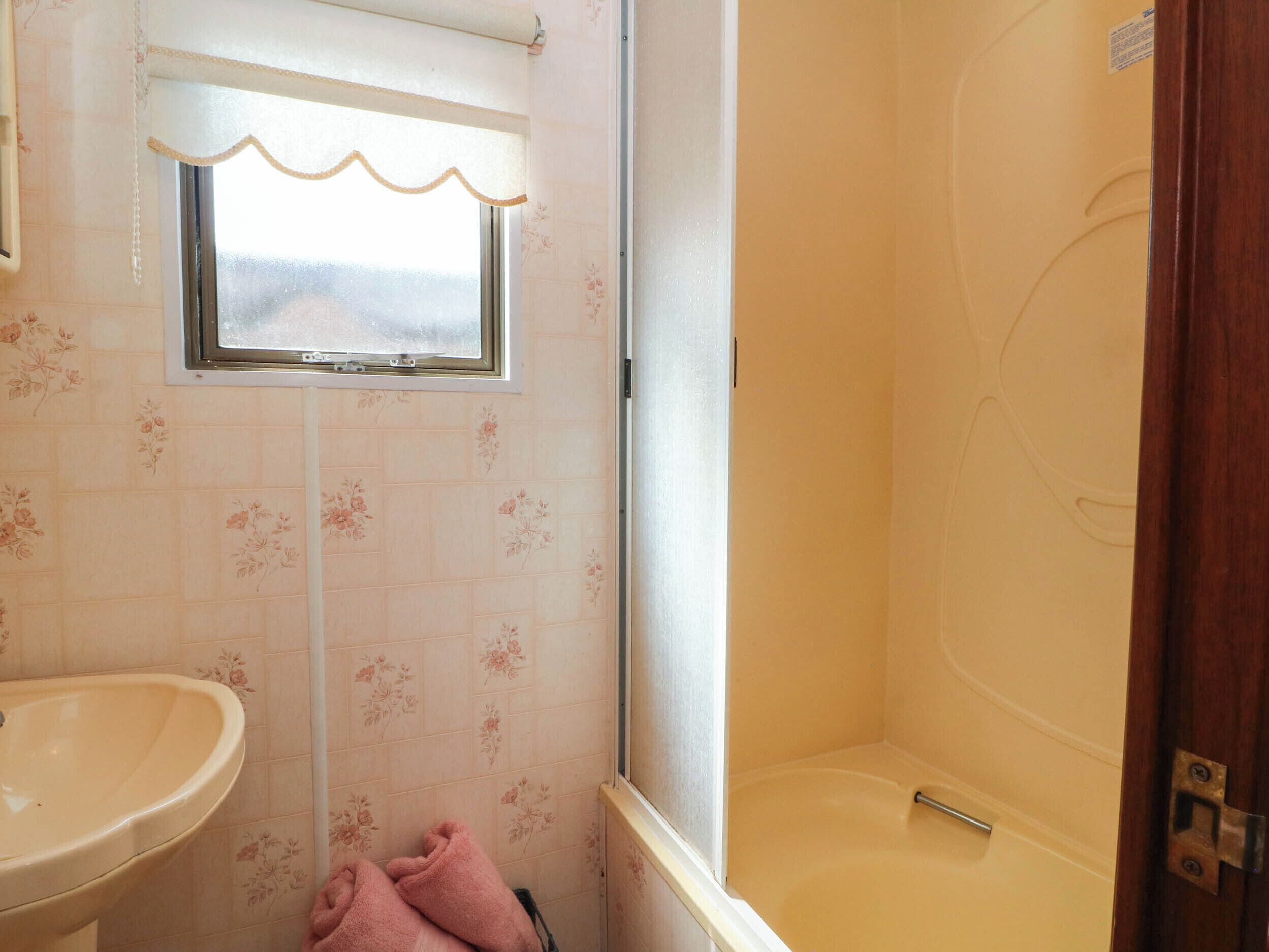 A bathroom with a sink, a window with a curtain, and a bathtub.