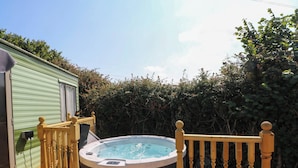 A hot tub on a wooden deck with a wooden railing and a green building in the background.