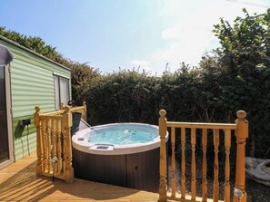 A hot tub on a wooden deck with a wooden railing and a green building in the background.