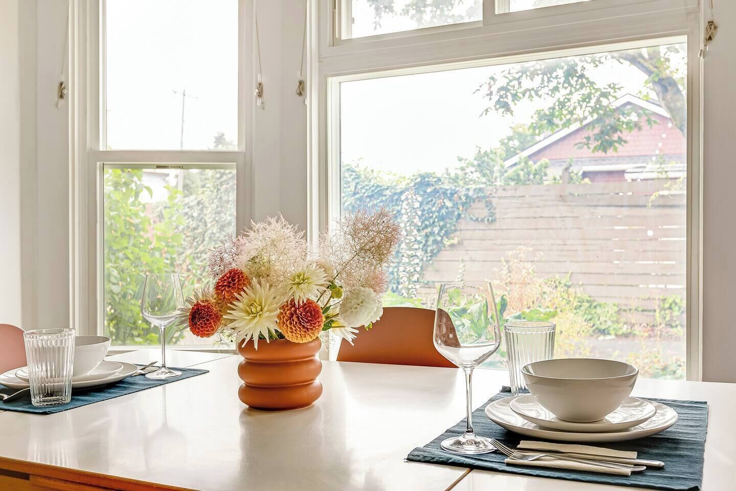 A dining table with a vase of flowers, a bowl, and cutlery.