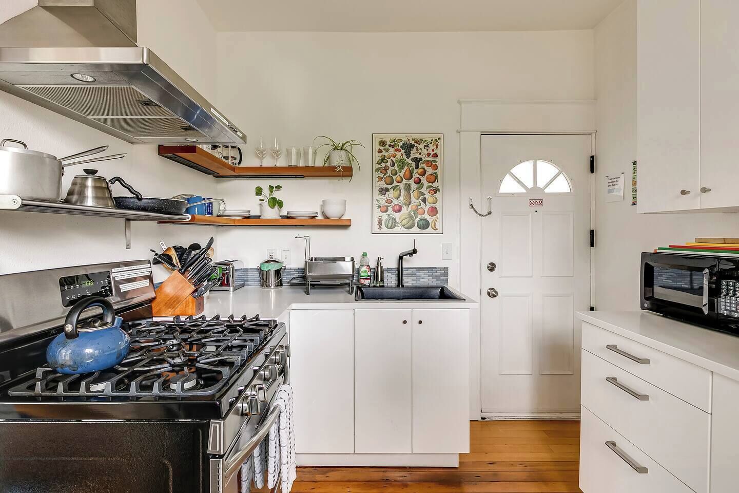 A modern kitchen with white cabinetry, a gas stove, a microwave, and a fruit-themed wall art.