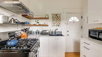 A modern kitchen with white cabinetry, a gas stove, a microwave, and a fruit-themed wall art.