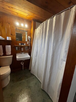 A bathroom with a toilet, sink, and shower curtain. - Cozy 1BR hotel room, Hamilton - #339 Dekonawada (Hamilton)