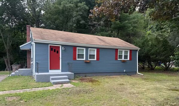 A small house with a red door, white shutters, and a brick chimney.