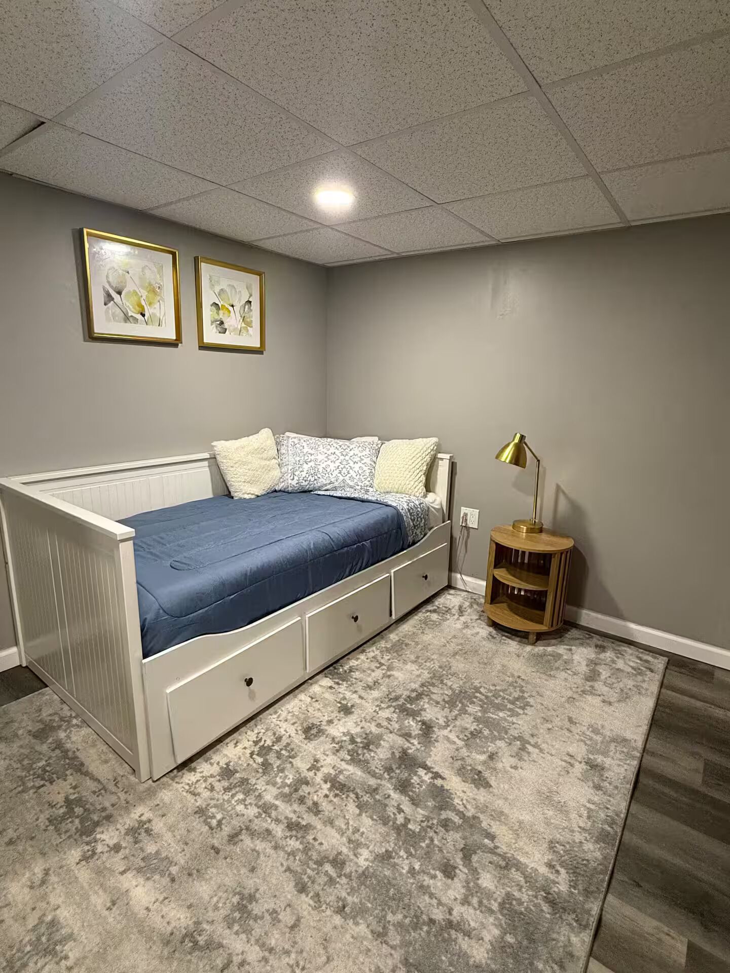 Un dormitorio con cama, mesita de noche, lámpara y dos cuadros en la pared.
