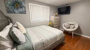A bedroom with a bed, a dresser, a chair, a television, and a window with blinds.