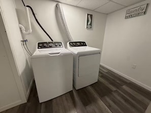 A laundry room with two white front-loading washers and dryers, a water hose, and a sign on the wall.