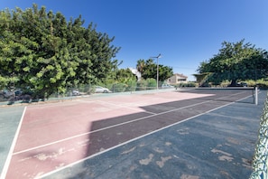 Ein Tennisplatz im Freien mit Netz, umgeben von Bäumen und einem Zaun.
