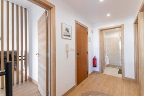 A hallway with wooden flooring, a fire extinguisher, and a framed picture on the wall. - Pool Apartment with Shared Pool, Private Terrace, and Wi-Fi (Tavira)