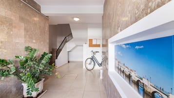A hallway with a staircase, a potted plant, a bicycle, and a mural of a bridge.