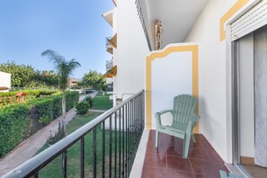 A balcony with a green chair, a tiled floor, and a view of a well-maintained garden. - Pool Apartment with Shared Pool, Private Terrace, and Wi-Fi (Tavira)