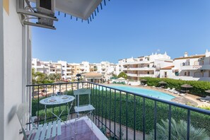 A balcony with a pool view, outdoor furniture, and a clear sky. - Pool Apartment with Shared Pool, Private Terrace, and Wi-Fi (Tavira)