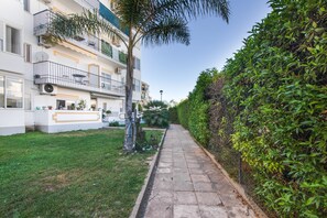 A pathway leading to a building with a white facade, balconies, and a neatly trimmed hedge on one side. - Pool Apartment with Shared Pool, Private Terrace, and Wi-Fi (Tavira)