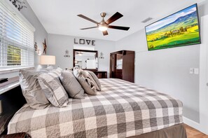 A bedroom with a checkered bedspread, a ceiling fan, a wall-mounted TV, and a window with blinds. - 2-bedroom house in adorable Largo with cool AC and charm (Largo)