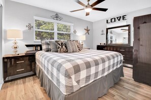 A bedroom with a bed, nightstands, a dresser, a ceiling fan, a window with blinds, and a wall with a word 'LOVE'. - 2-bedroom house in adorable Largo with cool AC and charm (Largo)