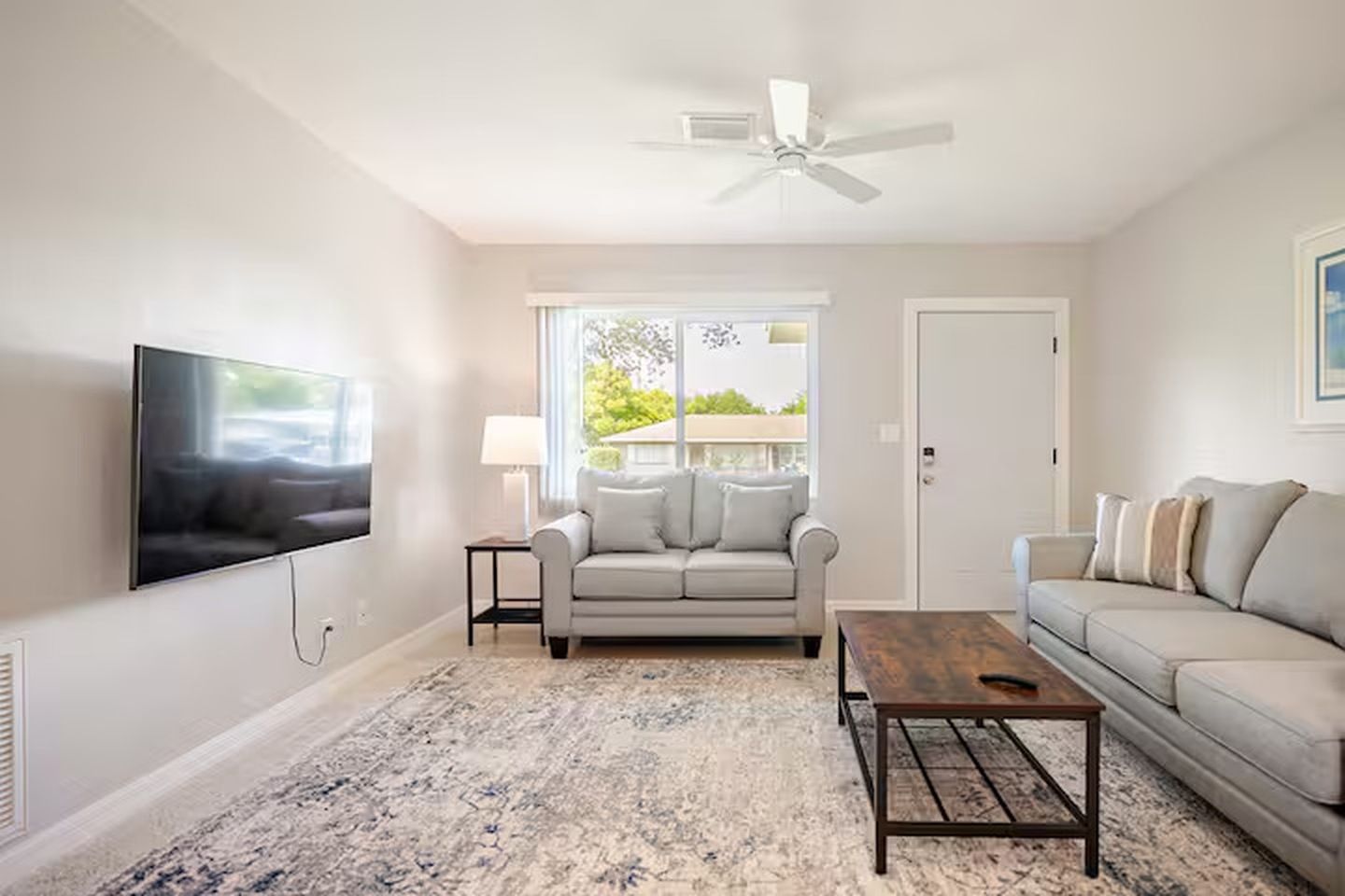 A living room with a flat-screen TV, a sofa, a coffee table, and a ceiling fan.
