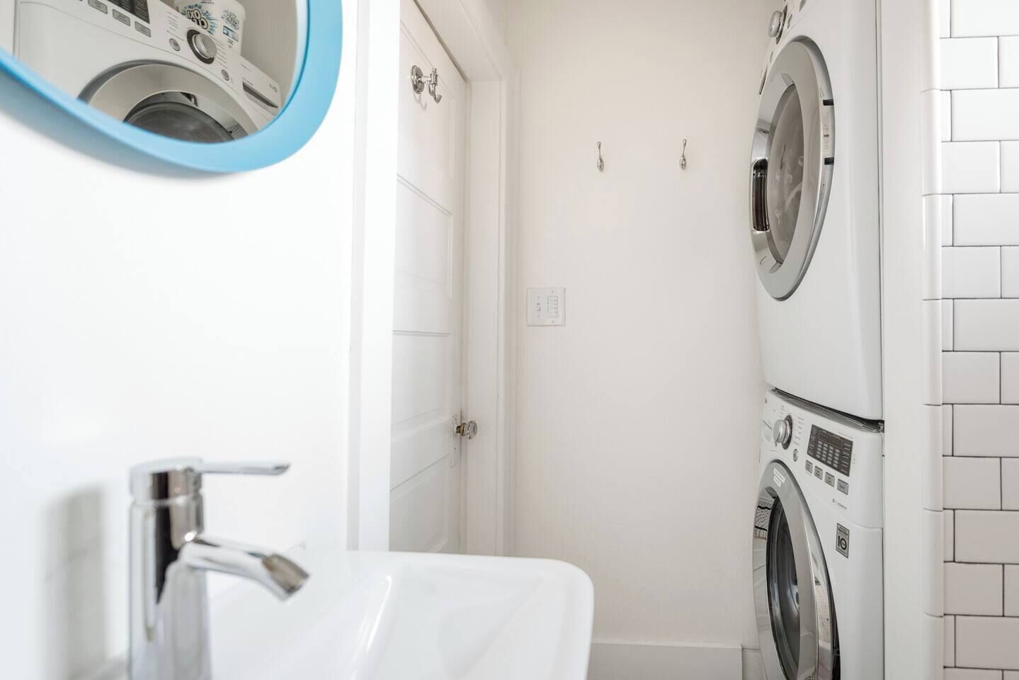 Une petite salle de bain avec un lavabo blanc, un miroir et deux machines à laver superposées.