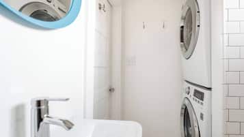 A compact bathroom with a white sink, a mirror, and two stacked washing machines.