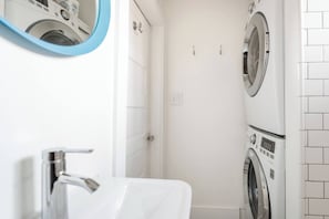A compact bathroom with a white sink, a mirror, and two stacked washing machines. - Radiant, Low-Key Apartment (Seattle)