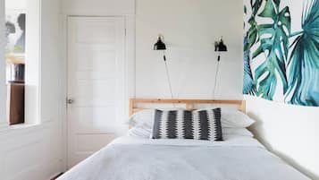 A bedroom with a bed, two wall-mounted lamps, a door, and a large tropical leaf painting.