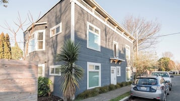 A two-story residential building with a grey siding exterior, a front door, and a small front yard with a palm tree.