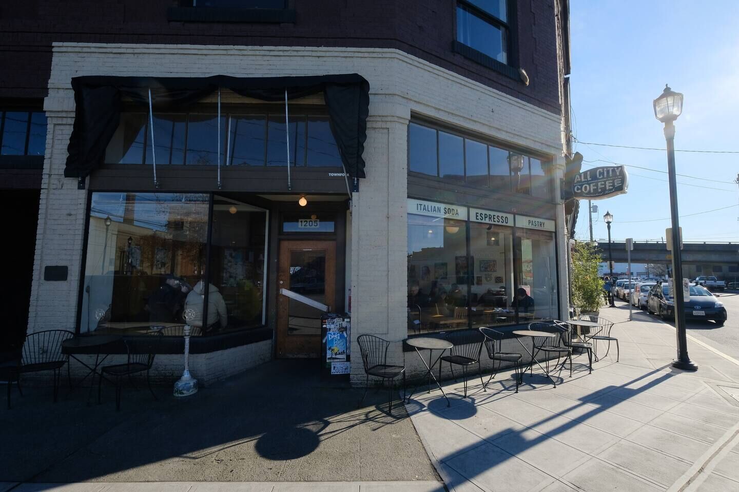 A corner building with a storefront labeled 'ALL CITY COFFEE' and a sign indicating '1205'.