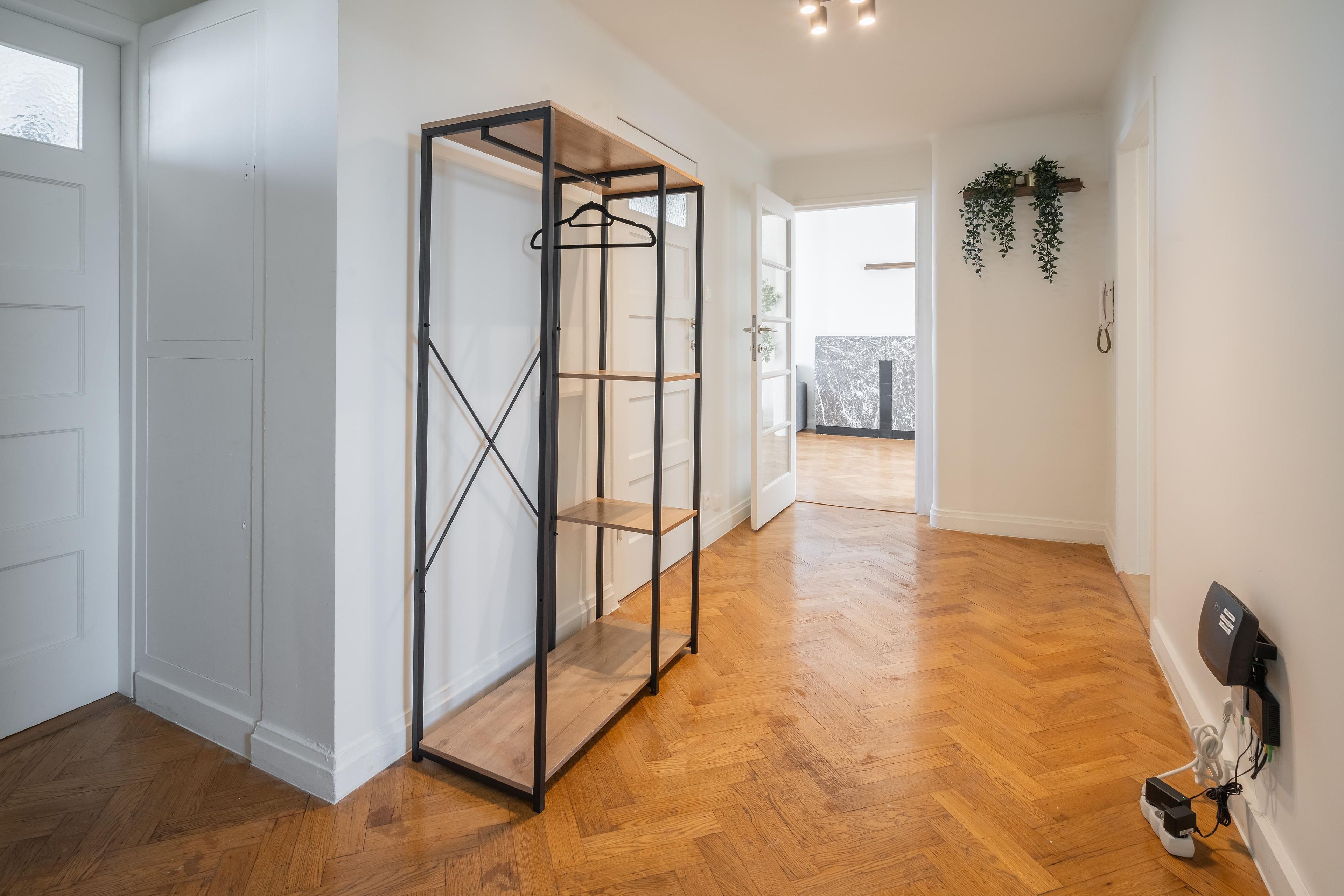 Un pasillo con suelo de madera, una estantería de estructura metálica y una puerta que da a un balcón.