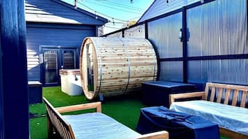 A rooftop lounge with artificial grass, wooden furniture, and string lights.