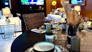 A dining area with a round table set for two, a pitcher, wine glasses, and a television displaying a sports event.