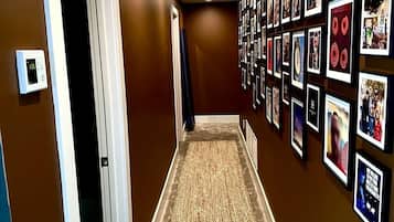 A hallway with a patterned carpet, a wall of framed pictures, and a door on the left.