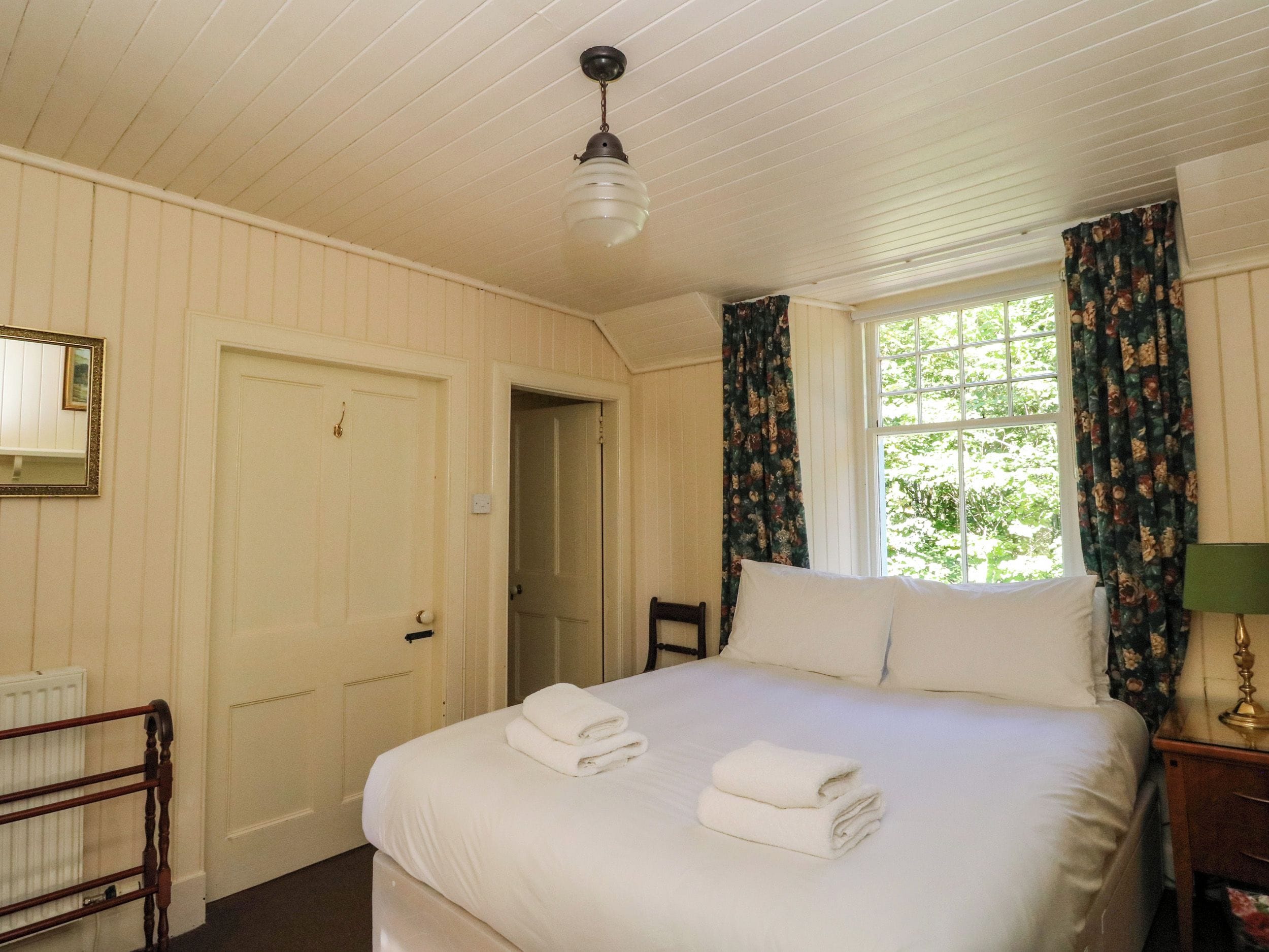 Habitación de hotel con cama, una silla, ventana con cortinas, radiador y puerta.