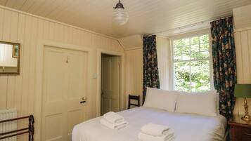 Habitación de hotel con cama, una silla, ventana con cortinas, radiador y puerta.