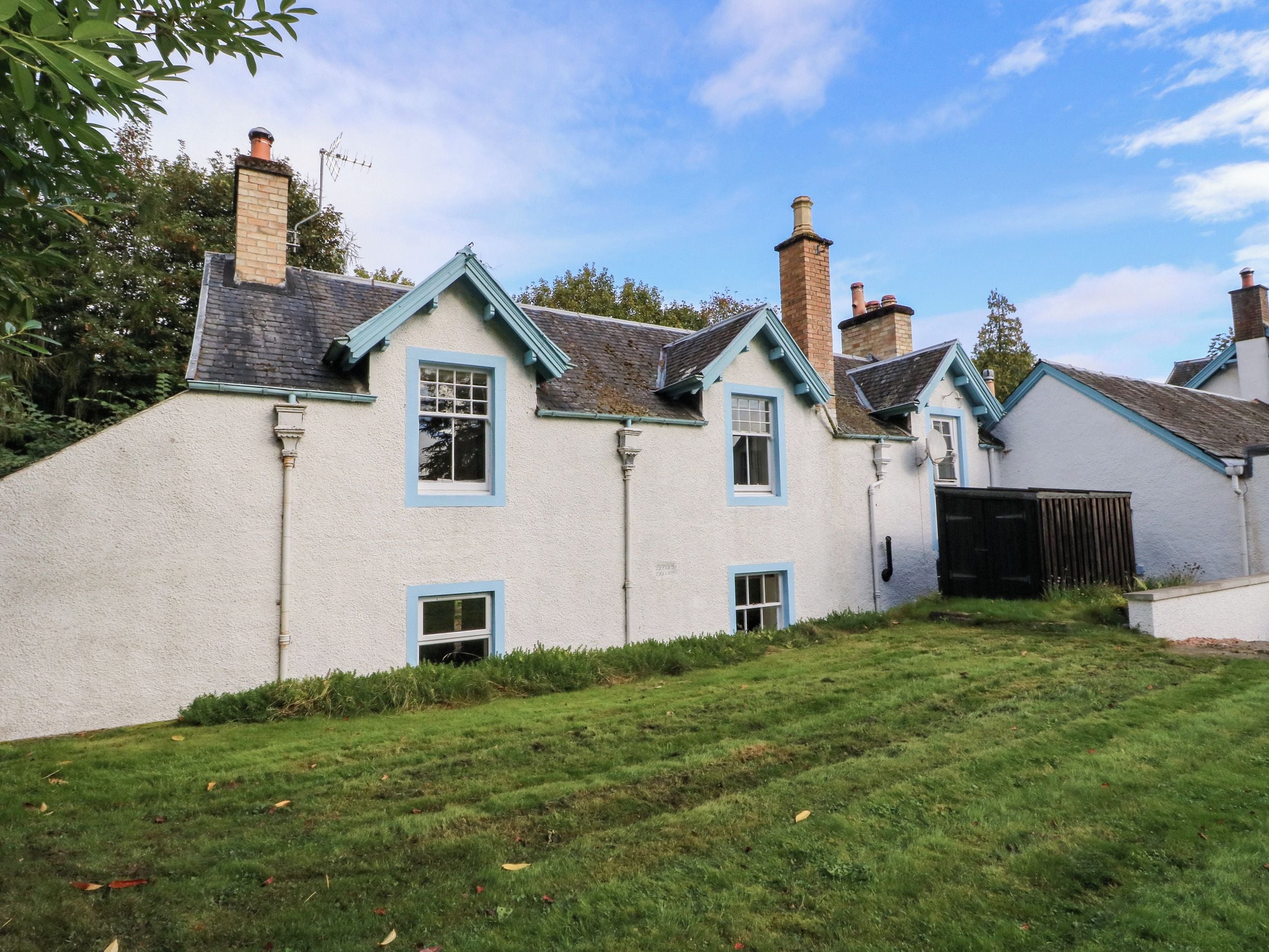 Une maison traditionnelle à l’extérieur blanc, dotée de plusieurs cheminées et d’une cour verdoyante.