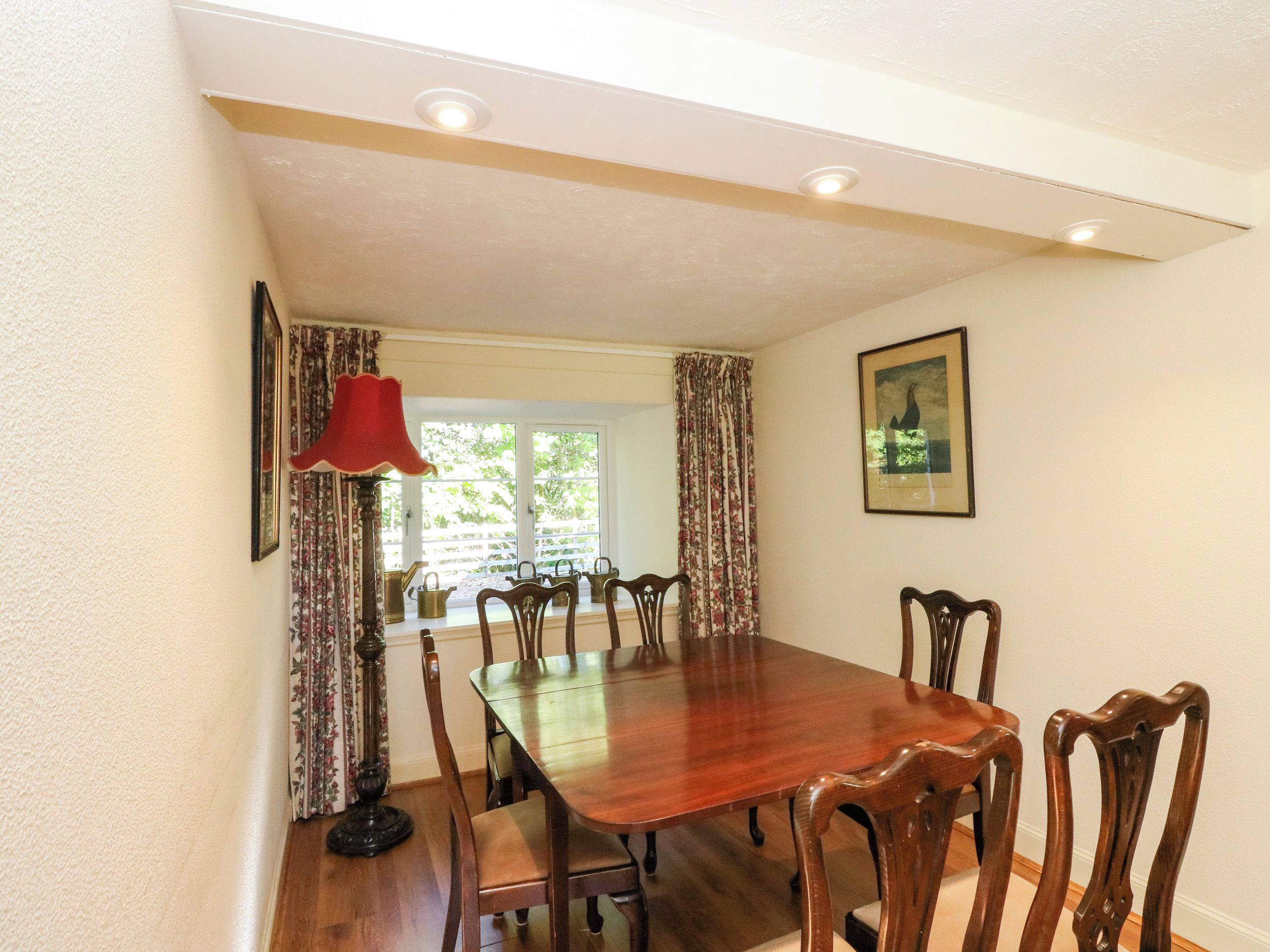 A dining room with a wooden table and chairs, a red lamp, and a window with curtains.