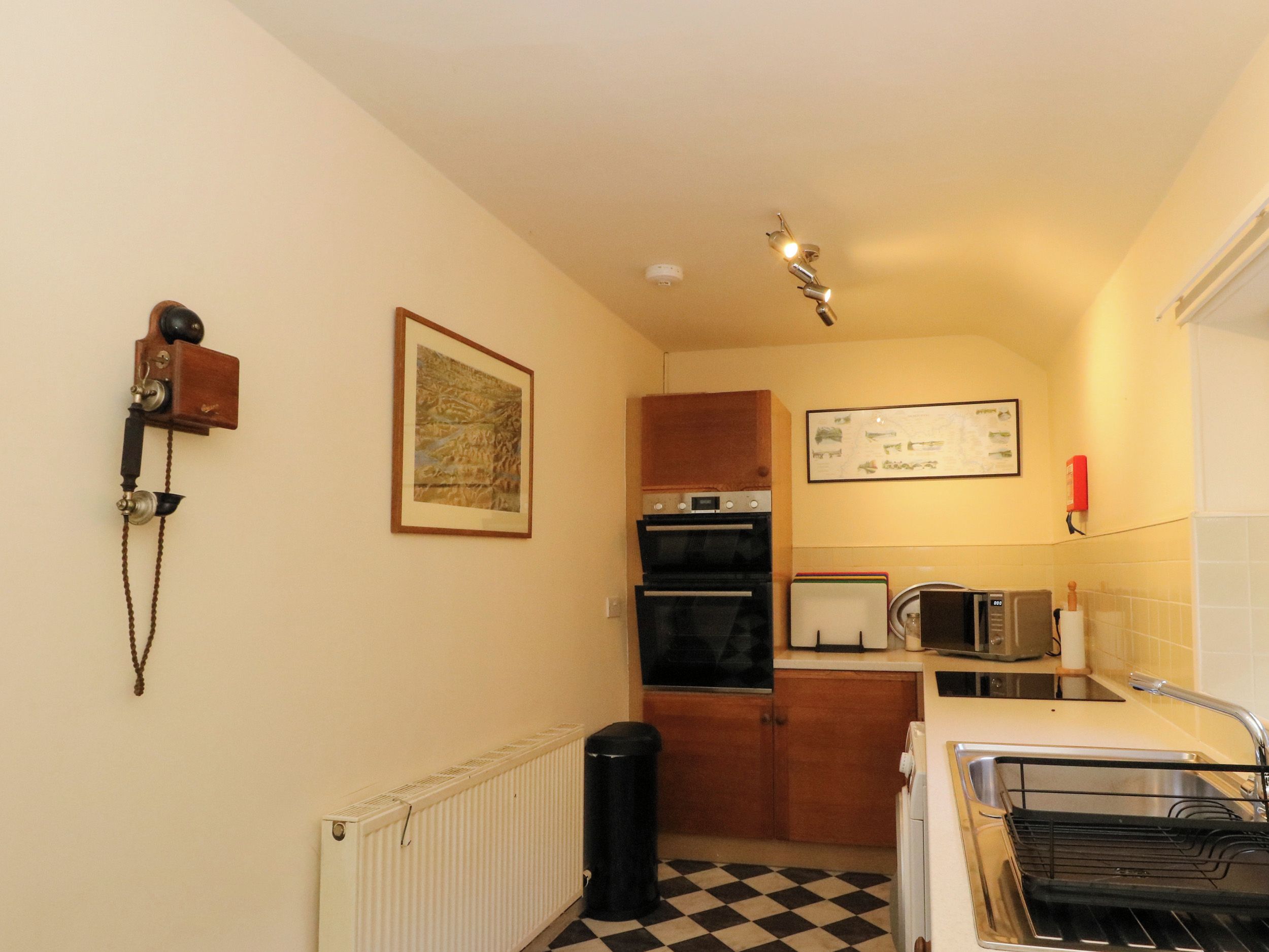 Una cocina compacta con un radiador, un basurero negro, un piso a cuadros y un microondas.