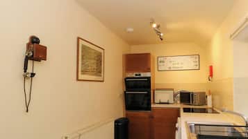 Una cocina compacta con un radiador, un basurero negro, un piso a cuadros y un microondas.