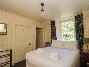 Une chambre d’hôtel avec un lit, une chaise, une fenêtre avec des rideaux, un radiateur et une porte.