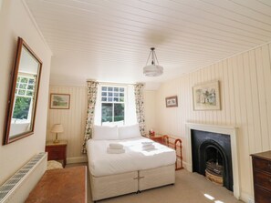 A bedroom with a bed, a fireplace, a window with curtains, a mirror, and a radiator.