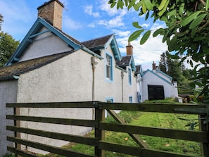A traditional house with a white exterior and blue trim, a wooden gate in the foreground, and a grassy yard. - Gardeners Cottage (Perth)