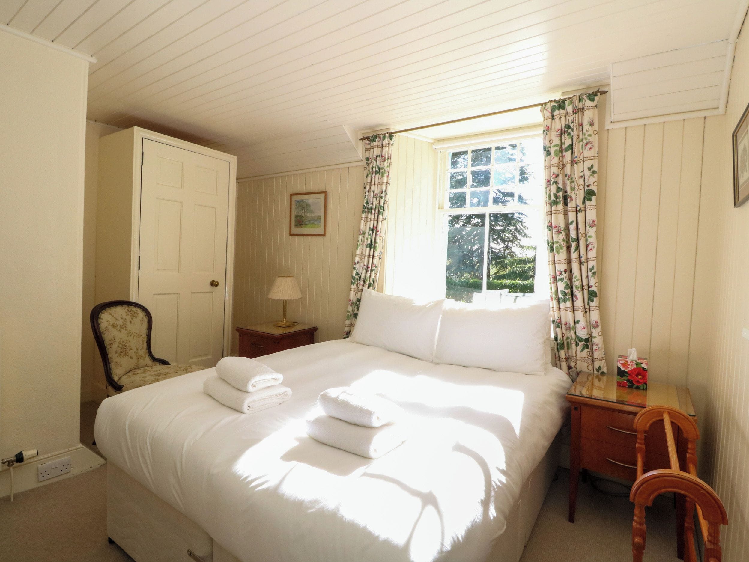 A bedroom with a bed, a chair, a nightstand, a lamp, and a window with curtains.