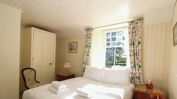A bedroom with a bed, a chair, a nightstand, a lamp, and a window with curtains.