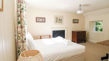 Une chambre à coucher avec un lit, une commode, une lampe, une cheminée et une fenêtre.